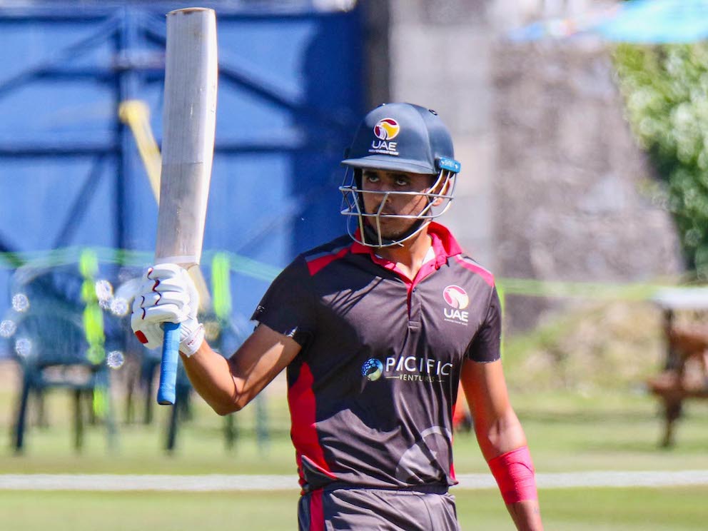 Aryan Lakra glances raises his bat on his way off after batting for UAE
